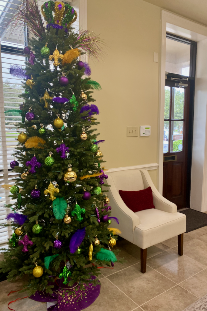 Christmas tree decorated for Mardi Gras in green, purple, and gold at a real estate brokerage