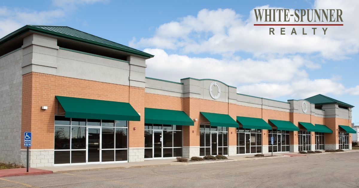 A modern brick and stone commercial retail strip center with green awnings, managed by White-Spunner Realty in Mobile, Alabama.