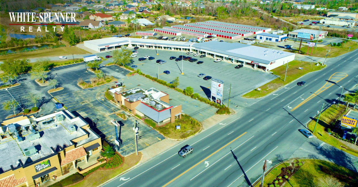 Aerial view of a small commercial retail strip center with tenant storefronts along a busy highway in Mobile, Alabama.